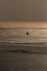samotny, mały jacht żaglowy płynący wzdłuż rafy koralowej otaczającej lagunę, na tle wschodzącego słońca nad oceanem indyjskim, Kenia, Afryka © Kamil_k2p