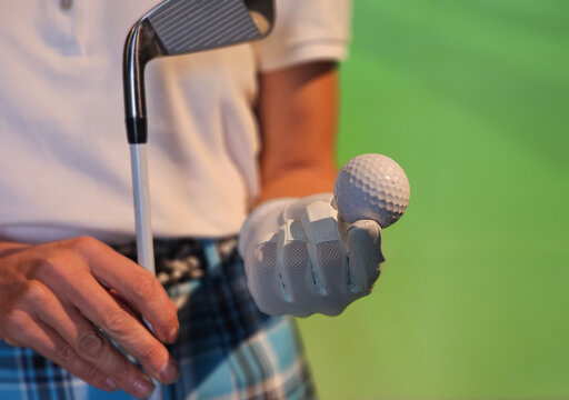 Golfer prepares for swing on green background holding a golf ball
