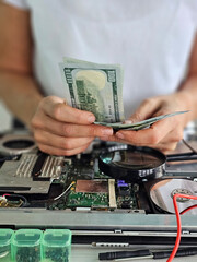 Hands are seen counting cash above an opened electronic device in repair workshop, with various tools scattered around the workspace concept