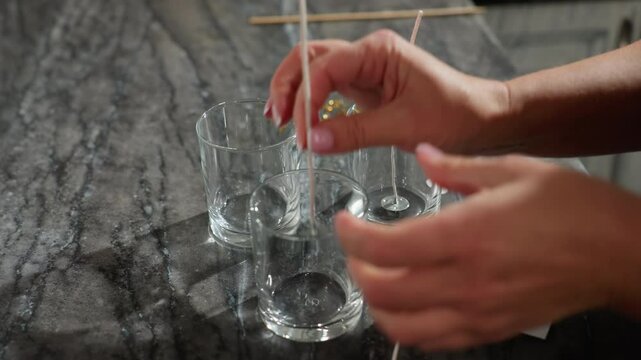 hand view of woman hand adorned with beads carefully handling and placing items with glass cups, beads, and tools on marble countertop in modern kitchen