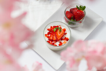 Top view of greek yogurt with strawberries on a white plate and cherry blossom