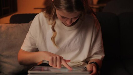Young girl  relaxing on home sofa, navigating digital tablet, browsing internet, play mobile games, reading e-books, engaging in online shopping during personal downtime
