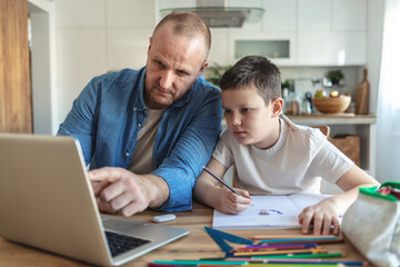 Obraz premium Shot of a young father using a laptop while his son does homework at home
