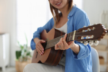 Fototapeta premium Young woman playing guitar at home, closeup