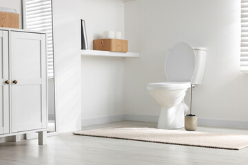 Toilet and brush near white wall in bathroom