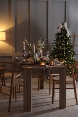 Christmas table setting with stylish dishware, glasses and burning candles in festive decorated room