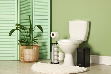 Ceramic toilet bowl, houseplant and necessities near green wall indoors