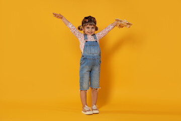 Happy little girl with toy plane on orange background