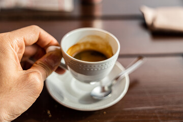 mano di giovane uomo adulto caucasico che regge una tazza bianca con del caffè espresso, al tavolo...