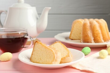 Pieces of delicious bundt cake, Easter eggs and tea on pink wooden table