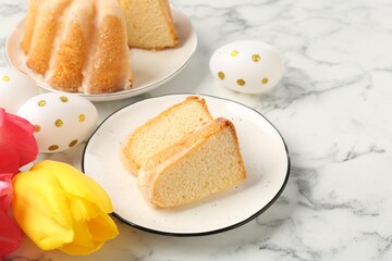 Pieces of delicious bundt cake, Easter eggs and tulips on light marble table, closeup