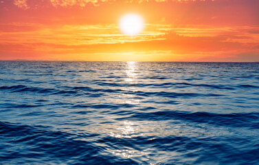 A serene ocean scene captures the golden sun setting over the horizon, casting a glowing path of light across the rippling blue waves.