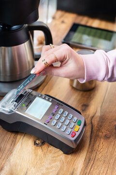 Woman's hand inserting credit card into Verifone POS terminal for payment at a cafe counter. Focus on transaction, cashless society, retail technology. Kyiv, Ukraine - January 26 2022
