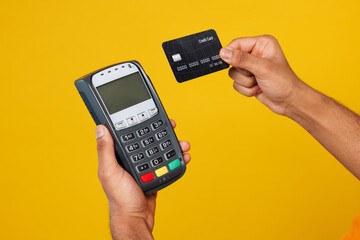 Close up cropped male hold in hand wireless bank payment terminal to process acquire credit card isolated on plain orange yellow wall background studio. Money concept. Copy space advertising mock up.