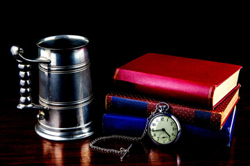 Vintage Pewter Tankard with Old Books and Pocket Watch on a Polished Wooden Surface