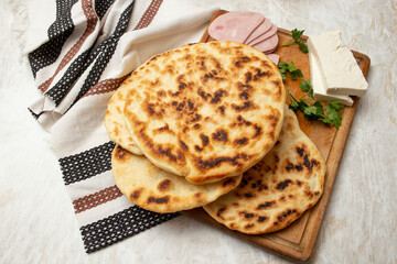 Fried pita bread stack on a wooden chopping board with ham slices and goat cheese, home made meal concept