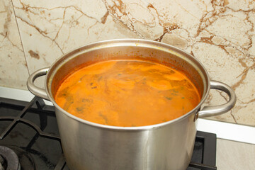 Meat ball soup, as romanian ciorba de perisoare in a steel pot ,steaming on gas stove