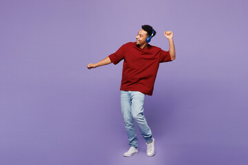 Full body young man of African American ethnicity wear red t-shirt casual clothes listen to music in headphones dancing isolated on plain pastel purple background studio portrait. Lifestyle concept.
