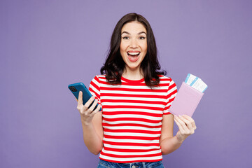 Traveler woman in red casual clothes hold passport ticket mobile cell phone isolated on plain purple background. Tourist travel abroad in free spare time rest getaway Air flight trip journey concept