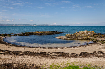 Large rock pool edged with seaweed formed by incoming tide at Helen's Bay with a view across Belfast Lough