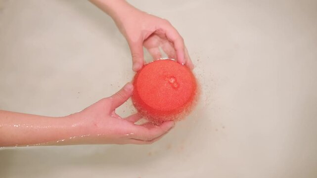 Pink bath bomb in her hands, foaming in the water, close-up. A place to copy	
