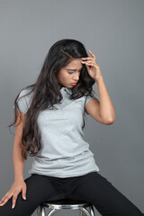 A confident woman dressed in casual business attire sits on a modern stool in a studio setup,...