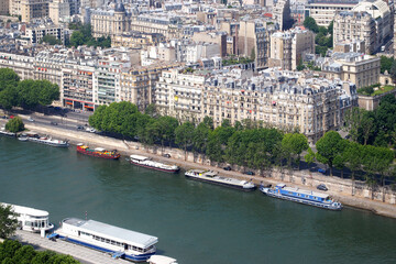View of the Seine embankment and moored pleasure boats from the top of the Eiffel Tower on a bright sunny day.