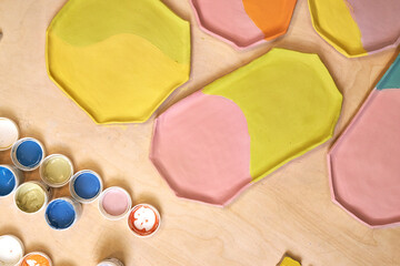 top view of handmade clay plates covered with colored glazes and glaze jars, ready for firing