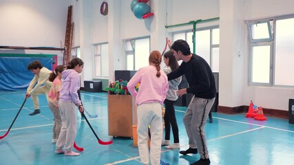 Elementary school students learning floorball skills during physical education class, playing together with energetic teamwork and enthusiasm in school gymnasium