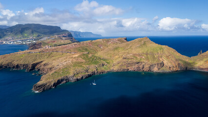 View of rugged coastline and lush hills surrounding a serene bay on a sunny day in Madeira Island, Portugal