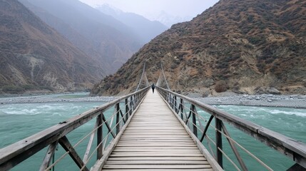 Obraz premium A trekker crosses a precarious suspension bridge over a rugged canyon river