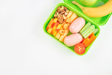 balanced lunch box with fresh fruits, vegetables, meat, and nuts on a light background, top view. copy space