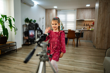 Young girl joyfully creating content in a modern kitchen setting while recording on a camera tripod