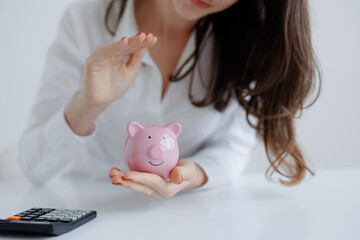 Woman saving money in a pink piggy bank while planning finances at a desk