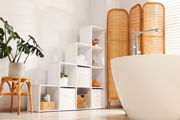 Stylish bathroom with shelving unit, bathtub and houseplants