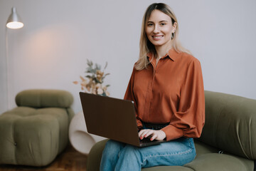 Young woman working on laptop while sitting comfortably in a cozy living room with stylish decor