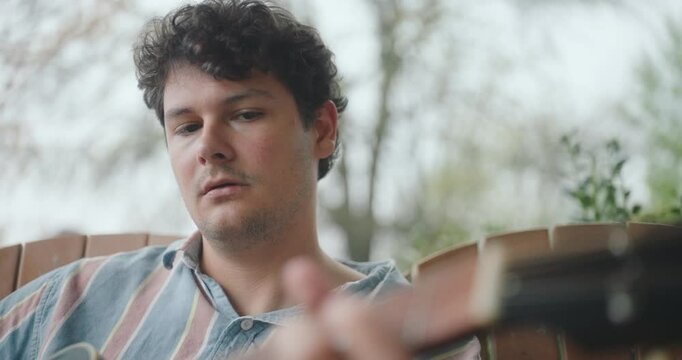 Young male musician sitting on a porch, playing guitar and writing a song