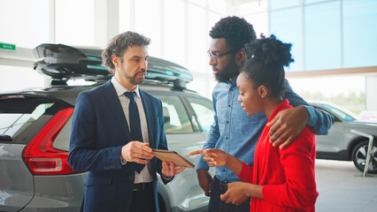 Beautiful married couple watching presentation of new car model on tablet device. Professional...