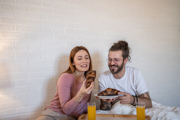 Happy couple enjoying breakfast with croissants and orange juice in bed