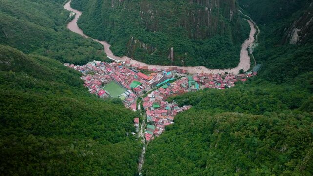 Aerial view of Aguas Calientes town nestled in a lush green valley near Machu Picchu, Peru, surrounded by dense forest and steep Andean mountains.