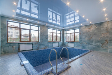 Private empty swimming pool with mirrored ceiling and beautiful decor. The pool bowl is decorated with blue mosaic tiles. Large windows overlook the courtyard.