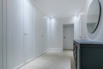 Elegant hallway design with white built-in wardrobes.  White room decor, spotlights, stylish furniture.