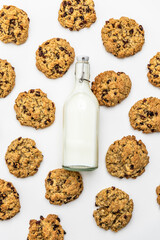 Flat lay of oatmeal raisin cookies with scattered oats and raisins and mik bootle on a white background. Ingredients and baked goods styled together. homemade bakery style