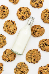 Flat lay of oatmeal raisin cookies with scattered oats and raisins and mik bootle on a white background. Ingredients and baked goods styled together. homemade bakery style