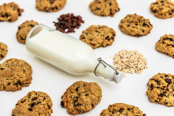 Flat lay of oatmeal raisin cookies with scattered oats and raisins and mik bootle on a white...