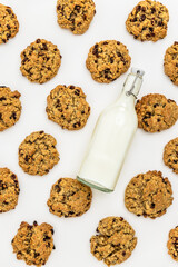 Flat lay of oatmeal raisin cookies with scattered oats and raisins and mik bootle on a white background. Ingredients and baked goods styled together. homemade bakery style