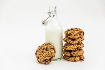 Glass bottle of milk with a stack of homemade oatmeal raisin cookies on a white background. Cozy and simple composition of traditional snack. Bakery style poster