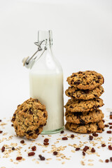 Glass bottle of milk with a stack of homemade oatmeal raisin cookies on a white background. Cozy and simple composition of traditional snack. Bakery style poster