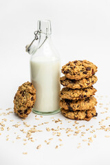 Glass bottle of milk with a stack of homemade oatmeal raisin cookies on a white background. Cozy and simple composition of traditional snack. Bakery style poster