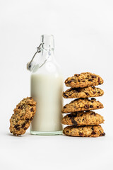 Glass bottle of milk with a stack of homemade oatmeal raisin cookies on a white background. Cozy and simple composition of traditional snack. Bakery style poster
